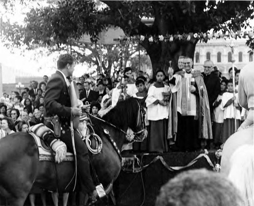 Man on horseback passing in front of priest