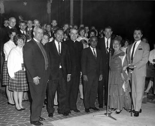 Gilbert Lindsey standing at the microphone with Mario Valadez, Consuelo Bonzo and group