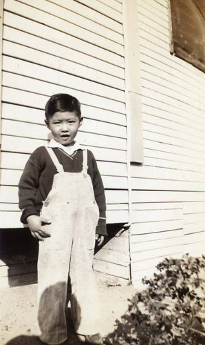 Ronald Siu at three years standing in front of a house