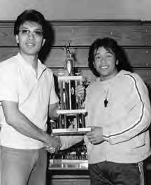 Two men holding a volleyball trophy in an indoor gym