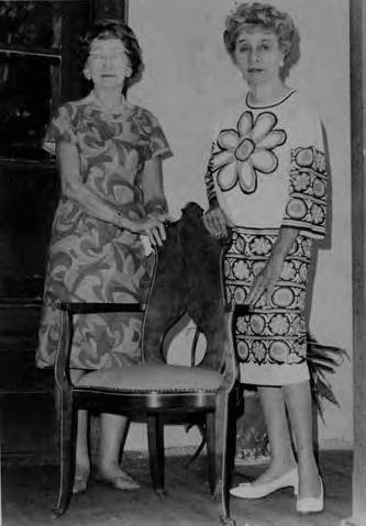 Two women standing next to a chair in the Avila Adobe