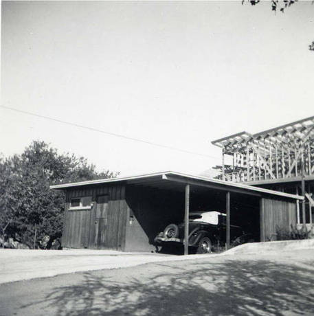 Parked car in a garage. The garage has an enclosed space as well as an open part, where the car is parked. On the back of the photo it reads "Ethel's house - our framing in back gr." (Spencer Chan Family)