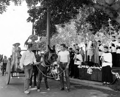 Men leading donkey cart past priest