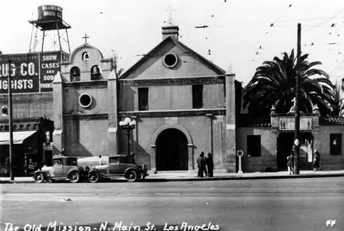 Plaza Church with car in front and Brunswig Drug Co. and water tower in the background