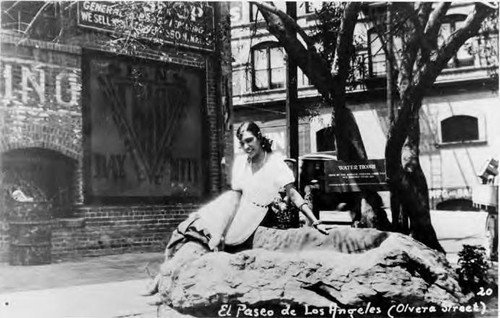 Postcard of girl sitting on water trough at north end of Olvera Street, Italian Hall at left