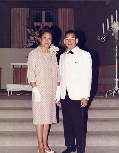 Mr. and Mrs. Poy Wong at their daughter's wedding, standing inside of a church