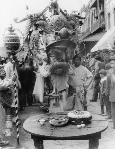 Giant Chinese New Year parade dragon in front of the Garnier Building after a performance. The dragon's orb is at frame left and an offering table at the center foreground holds teacups and dishes with food