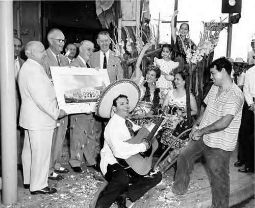 Guitar player in front of men, men holding picture of Simpson Building at corner of Main and Sunset Streets