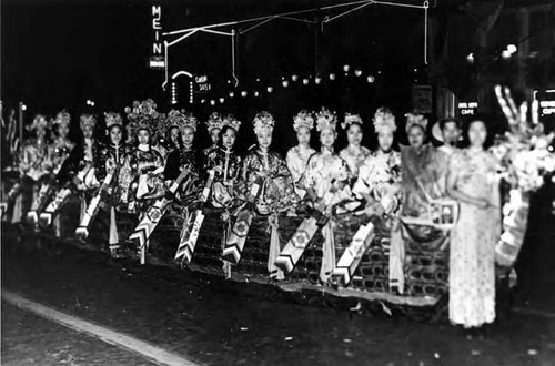 A side view on the left side of the women participating in the Moon Festival. They are riding on a dragon. In the background there is a Chop Suey restaurant and a cafe