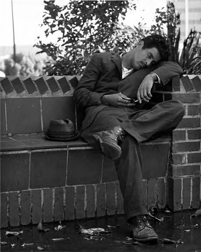 Man sleeping on brick bench in plaza near kiosko