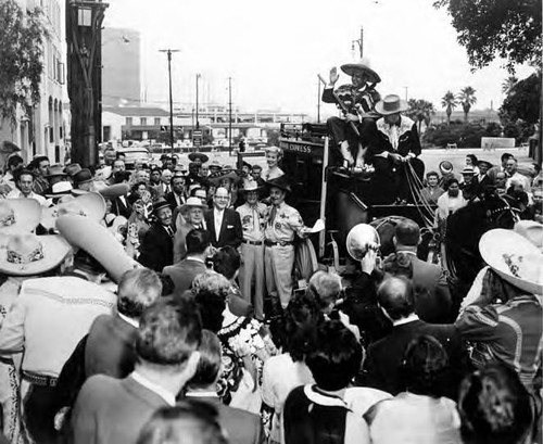 Crowd surrounding a stage coach that Sheriff Pitchess is sitting on top of in front of the Simpson building