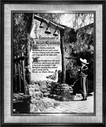 A photogrpah of a man standing on Olvera Street, reading a poster in Remembrance of Harry Chandler