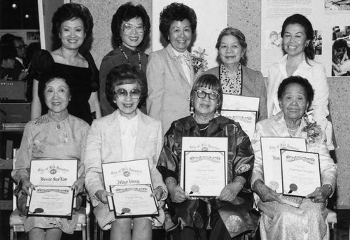 In the seventies began the organizing of the new and vigorous Chinese Historical Society of Southern California. One of the early programs was to recognize the pioneer women of Los Angeles. This photograph is of the honorees of which include Dolores Wong, standing in the middle, and Lily Lum Chan, sitting in the middle