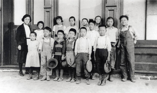 Jue Family in San Fernando, 14 children standing inside with an older woman on the left (perhaps the mother). The boys have taken their hats off