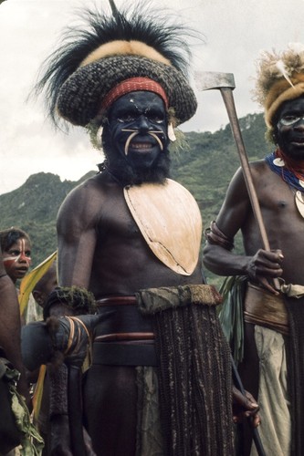 Decorated man, dressed for a ceremonial parade and display, wears headdress with cassowary feathers and a large baler shell