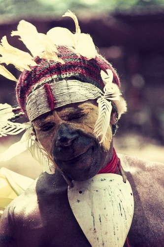 Villager, perspiring and fatigued, wears feathered looped headdress with trade-bead headband, face paint and baler shell valuable