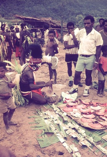 Pearlshells (smeared with red pigment) and Australian currency are prepared for ceremonial exchange, as a mission convert looks on