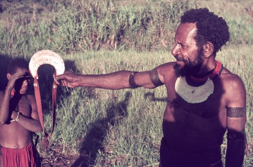 Holding an especially fine pearlshell to glint in the sun, man wears woven armbands and pearlshell pendant