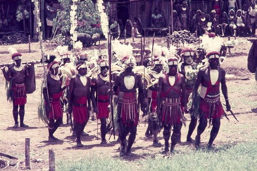 Visiting decorated participants parade in ritual finery, carrying banners of currency