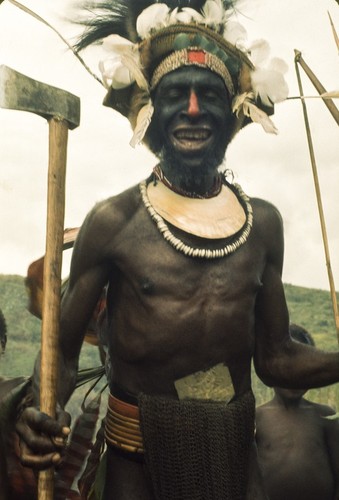 Dancer during a ceremonial gathering, in regalia, including headdress with feathers, nassa and kina shell valuables, and face paint