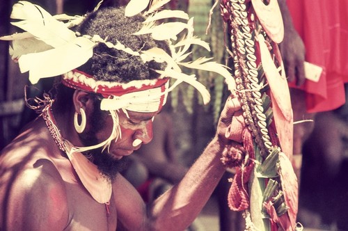 Decorated man holds up pearlshells and other valuables for ceremonial exchange