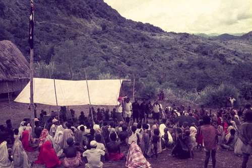 Patrol officer (center, in red cap) with his translator addresses villagers, Australian flag on pole at left