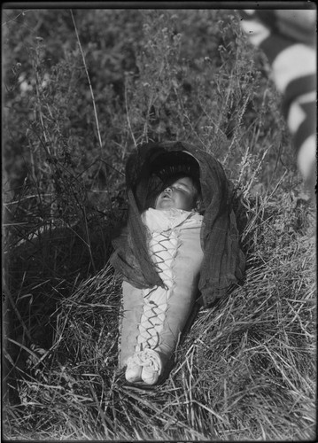 Paiute baby in cradle-board, laying in grass