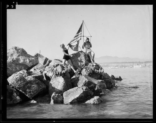 Two women posing with flag on breakwater at the Yacht Harbor Breakwater dedication, Santa Monica