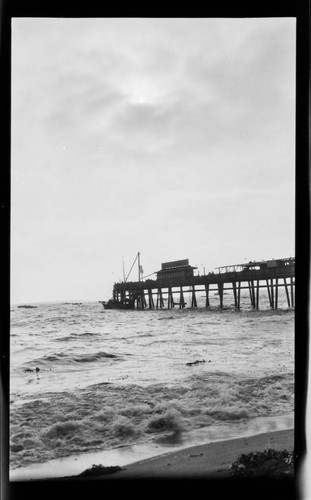 Short pier seen from shore with boat and people at end