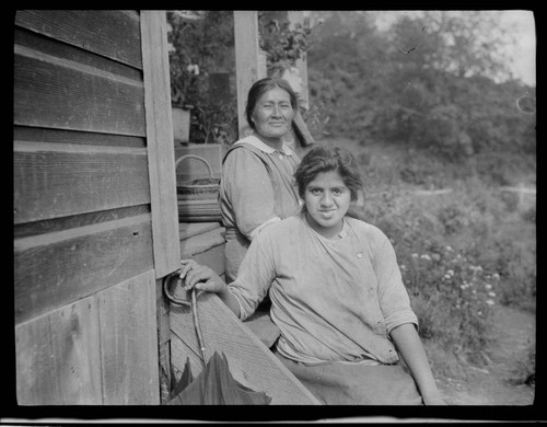 Two unidentified Native American women sitting on steps of a house