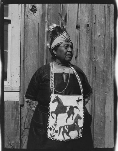 An unidentified Native American woman wearing beaded apron and feathered headdress