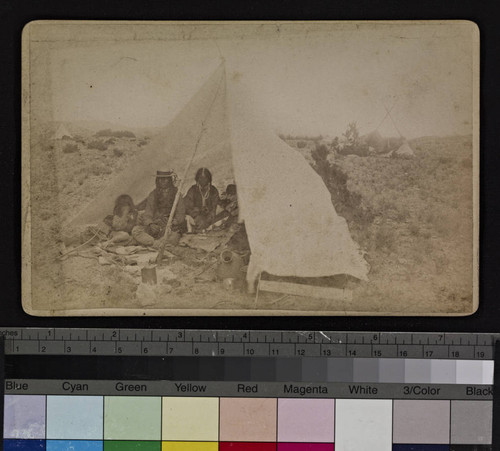 A group of Indians sitting beneath a tent shelter, with desert surroundings