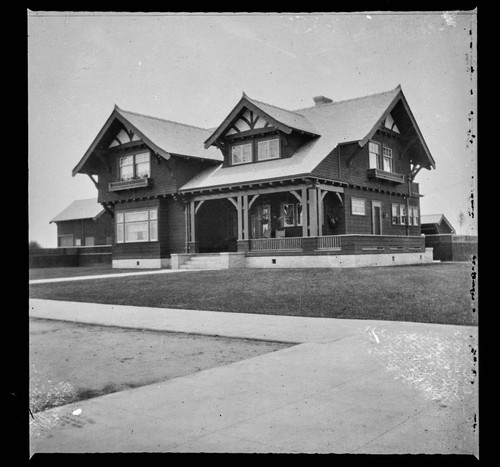 Unidentified two-story house with large lawn and new trees, street view