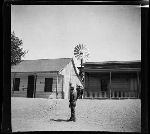 Men next to two wooden buildings, with windmill in background