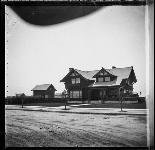 Unidentified two-story house with large lawn and new trees, street view