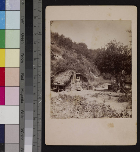 An Indian woman standing outside brush dwelling, San Gabriel, California