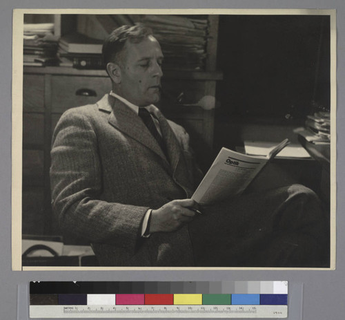 Portrait of Edwin Powell Hubble seated at a desk, reading