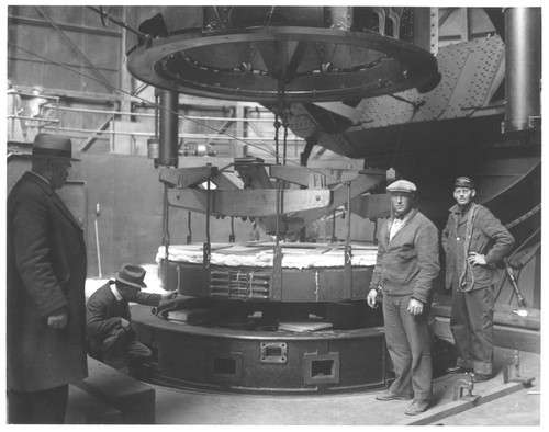 Four men posed with the 100-inch telescope mirror in its hoisting device, Mount Wilson Observatory