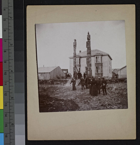 Totem poles standing in front of two-story building, Fort Wrangell, Alaska