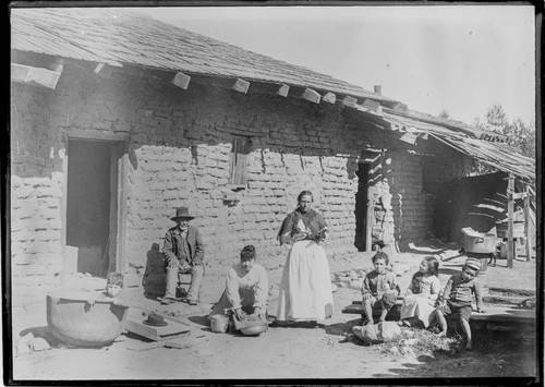 [Mexican] family outside adobe. One of the women is making tortillas