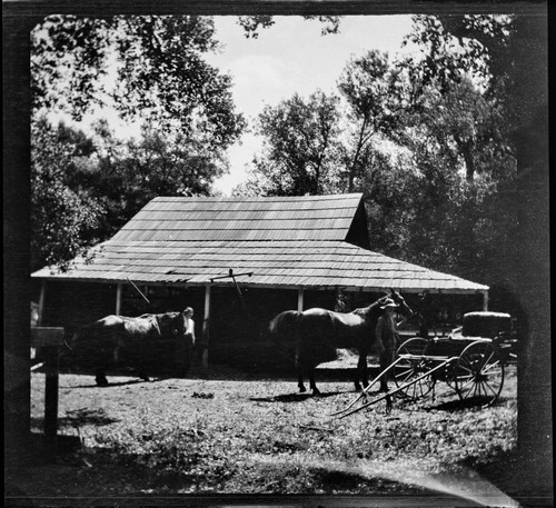 People with two horses near a carriage and stable(?)