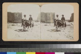 Two Pueblo Indian men on horses, with stone building in background