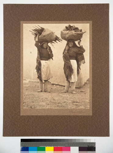Two young women of Isleta Pueblo carrying bundles of wood on their heads
