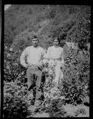 An unidentified Native American man and woman standing in a garden, with house in background