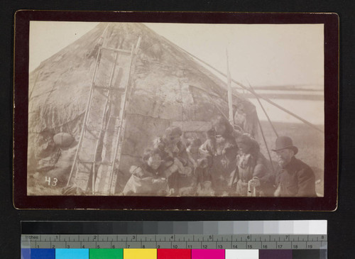 Caucasian man with Alaska natives in front of native house