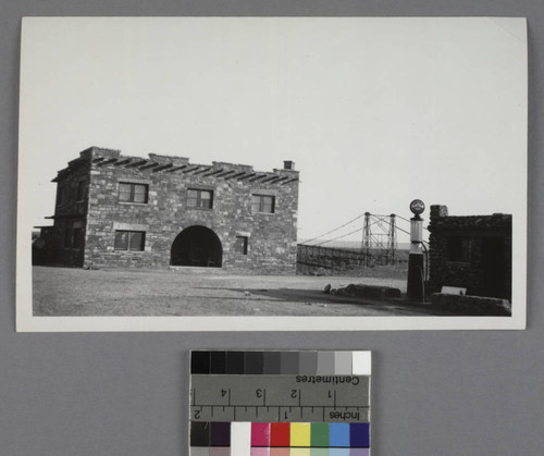 A stone pueblo building, with a service station in the foreground and a bridge in the background, Cameron, Arizona