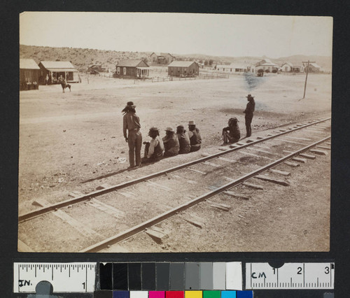 Native American men seated along railroad tracks in unidentified town