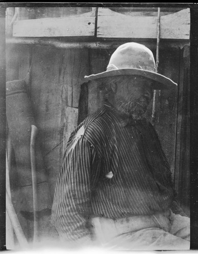 Native American man sitting in front of a wooden building