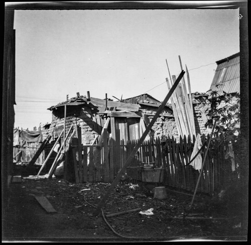 Adobe building held up by boards, with washing basin in yard