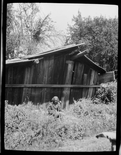 Native American man in front of a wooden plank house